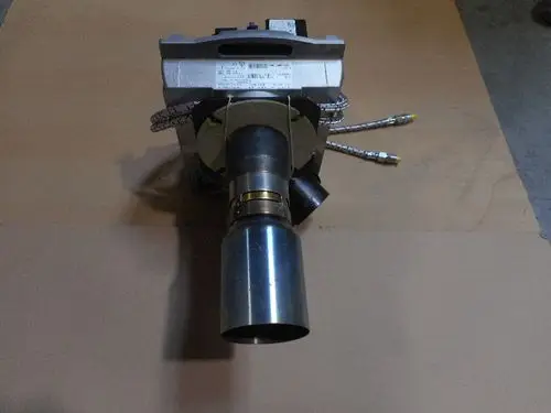 Brenner der Marke Remeha mit metallischem Auslass und Anschlussleitungen, montiert auf einer planar geformten Unterlage.